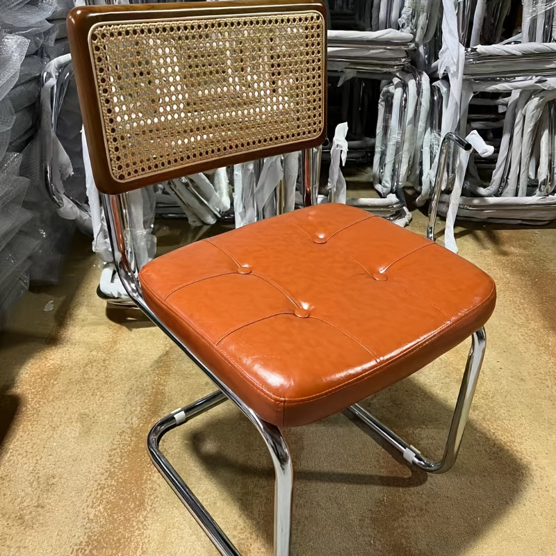 Una silla de comedor ergonómica hecha de ratán, con asas y asiento ajustable, perfecta para uso en patio y hogar. Se utiliza manualmente, tiene un respaldo robusto y es fácil de limpiar localmente, lo que la hace adecuada para adultos y ideal para suelos